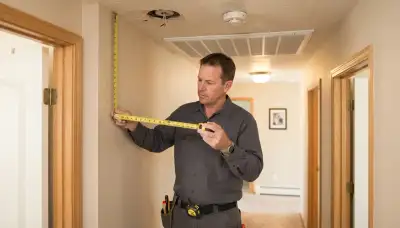 Electrician measuring ceiling and wall clearances for smoke detector installation in an Ogden, UT home